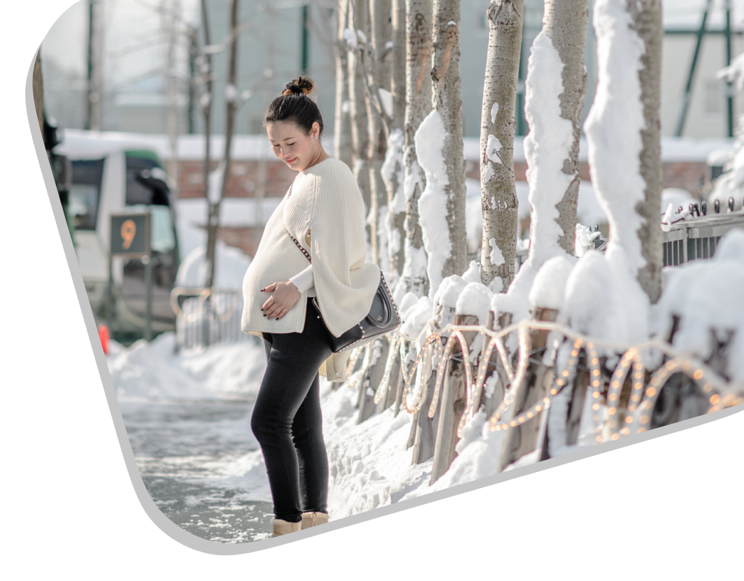 Pregnant Asian woman heading to a pregnancy massage London, standing outdoors beside a tree.