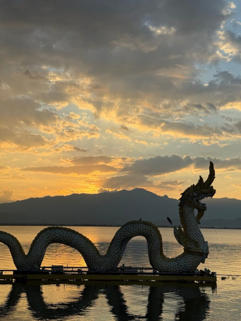 Sunset over a peaceful lake in northern Thailand featuring traditional dragon sculptures and tranquil natural scenery.