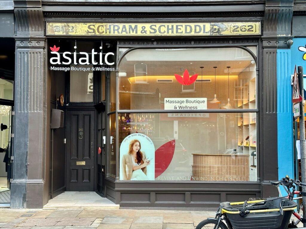 Exterior of Asiatic Massage Boutique London, with a warm sandy-colored historic building and signage reading 'Massage Boutique. & Wellness.