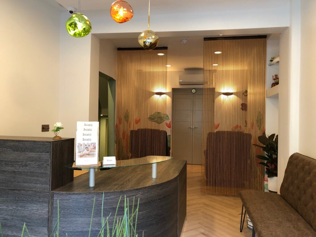 The reception area features Lotus-flower wallpaper and a foot massage chair for clients seeking Thai foot massages.