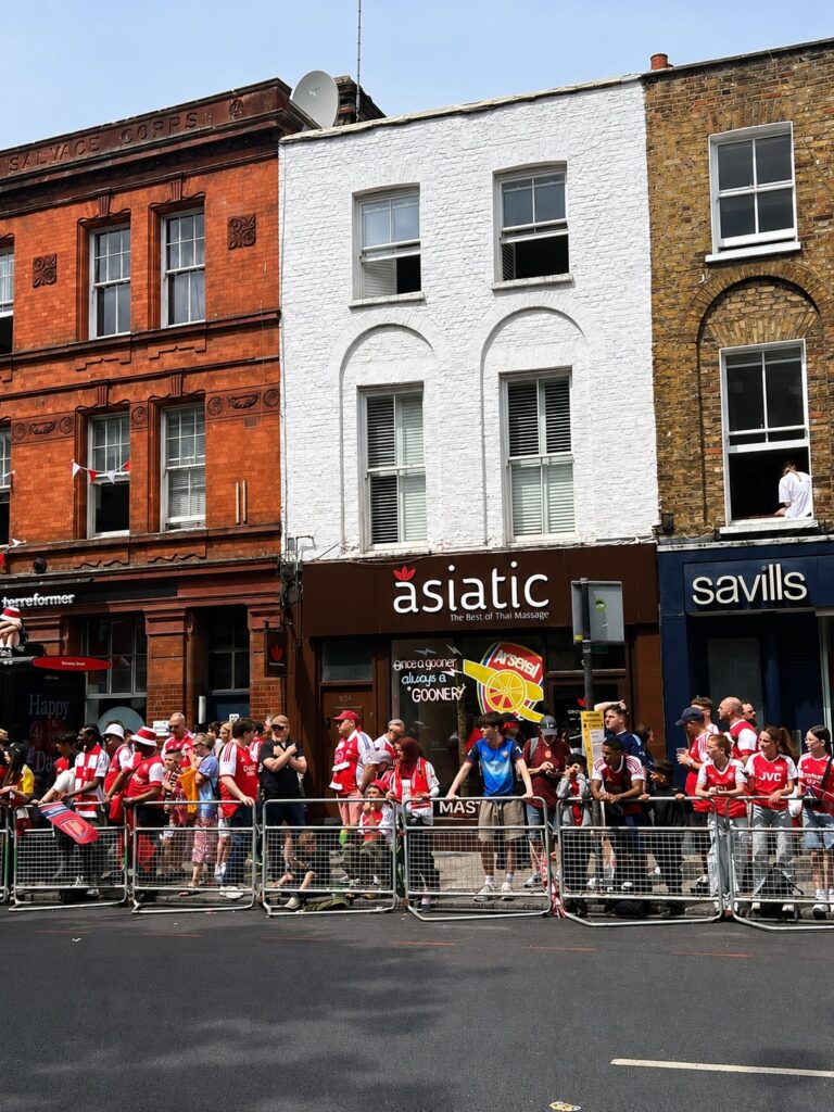 Asiatic 93 Upper Street storefront with Arsenal fans outside and hand-drawn cannon tribute on the window.