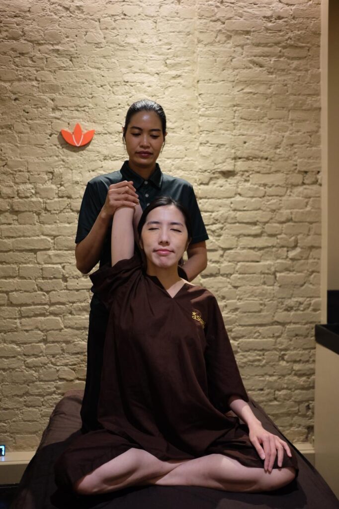 A Thai massage therapist performing an assisted shoulder and arm stretch to relieve muscle knots and tension in Islington, London.